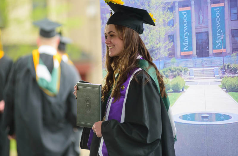 A young woman smiling holding her diploma in a cap and gown.